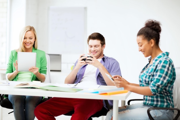 onderwijs, technologie en internet - studenten kijken naar telefoons en tablet-pc op school