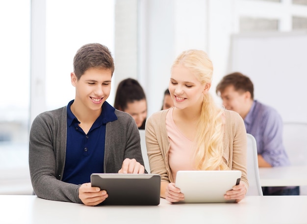 onderwijs, technologie en internet - twee lachende studenten kijken naar tablet-pc in lezing op school
