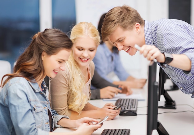 onderwijs, technologie en internetconcept - groep lachende studenten met computermonitor en smartphones