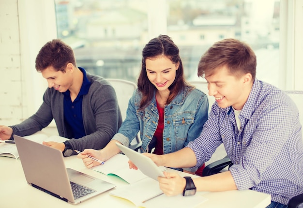 onderwijs, technologie, school en internet concept - drie lachende studenten met laptop, tablet pc en notebooks op school