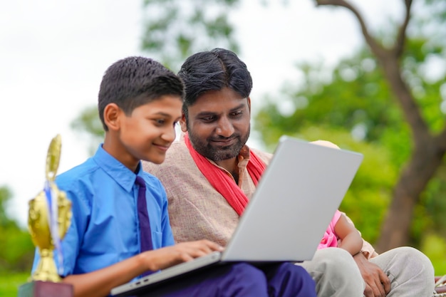 Onderwijsconcept: schattige Indiase schooljongen die laptop gebruikt en wat informatie geeft aan zijn vader.