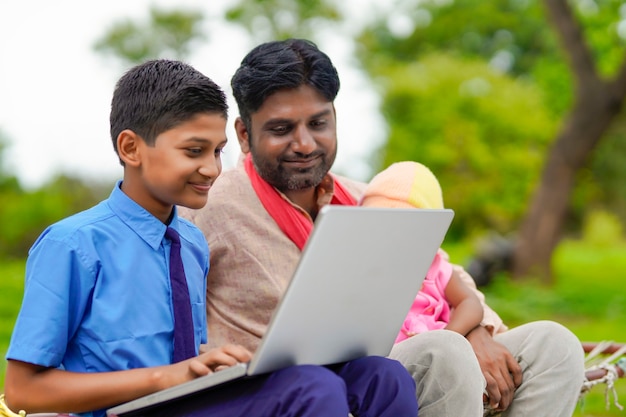 Onderwijsconcept: schattige Indiase schooljongen die laptop gebruikt en wat informatie geeft aan zijn vader.