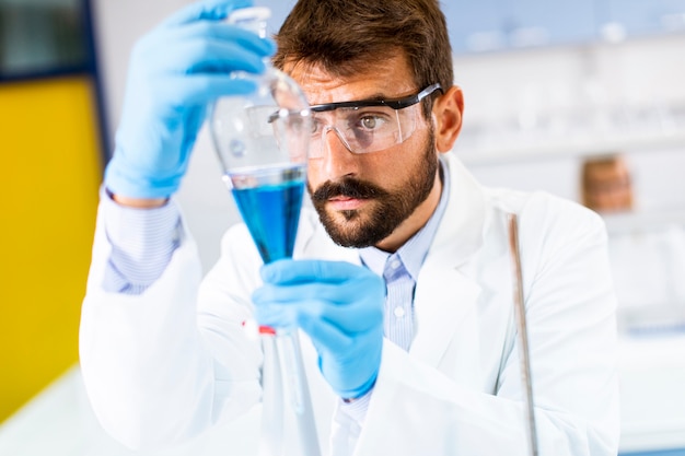 Onderzoeker die met blauwe vloeistof bij scheitrechter in het laboratorium werkt