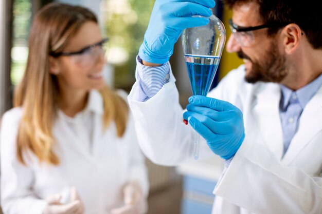 Onderzoeker die met blauwe vloeistof bij scheitrechter in het laboratorium werkt