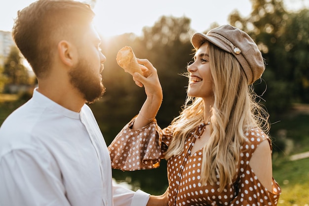 Ondeugend blond meisje met beige pet probeert de neus van haar vriendje te bevlekken met ijs Vrouw en man lachen en spelen in het park