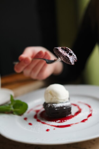 Ondiepe diepte van foeld foto van brownie cake met ijs. Hand van meisje met vork.