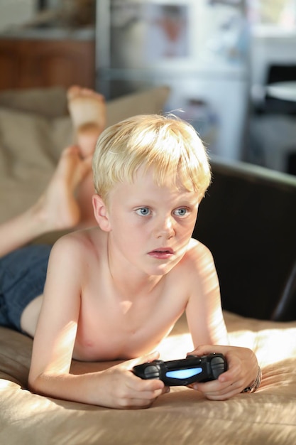 Ondiepe focus van een jongen met blond haar die op het bad ligt en computerspelletjes speelt met een joystick