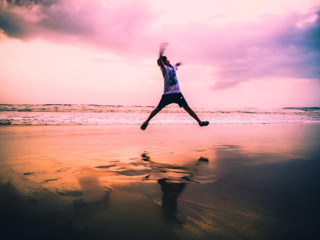 Foto onduidelijke beweging van een man die tijdens de zonsondergang op het strand op het land springt