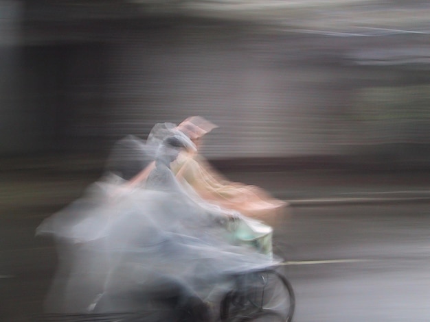 Foto onduidelijke bewegingen van een persoon die een regenjas draagt terwijl hij op straat fietst