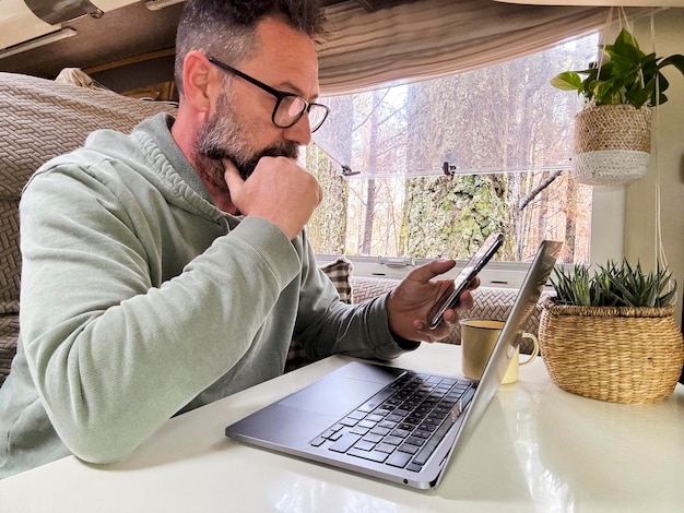 Photo one adult man using a laptop inside a camper van in vanlife remote worker digital nomad lifestyle small online business people concept mature male with beard and glasses use computer indoor nature