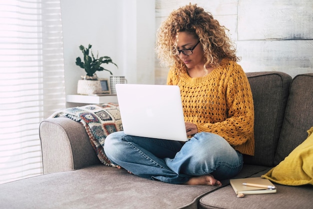 One adult modern woman at home working on laptop alone sitting on the sofa inside apartment Indoor technology leisure activity female people surfing the net on notebook computer Smart working relax