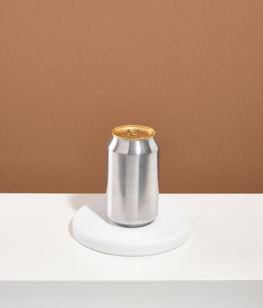 One aluminum can of a refreshingly cold drink stands on a white round stand on brown background