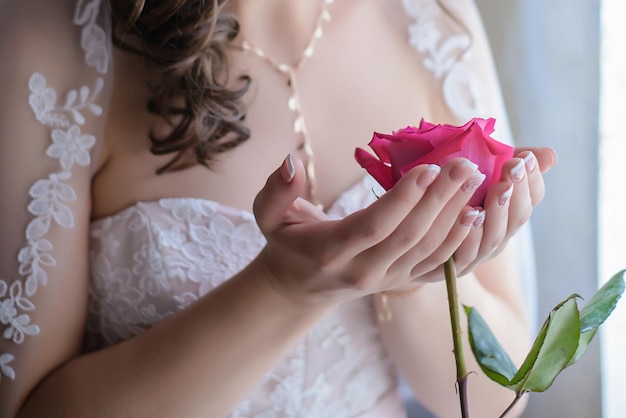 One beautiful pink rose in the hands of the bride on the wedding day closeup