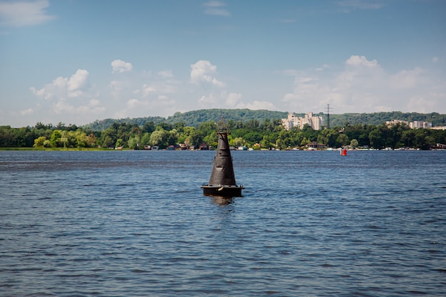 One black buoy on a calm water surface. Warning sign on the water on a sunny day.