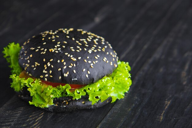 Foto un hamburger nero su una parete di legno scuro