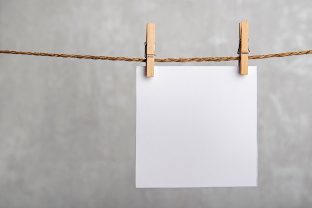 One blank square note paper card hanging with wooden clip or clothespin on rope string peg. Copy space.