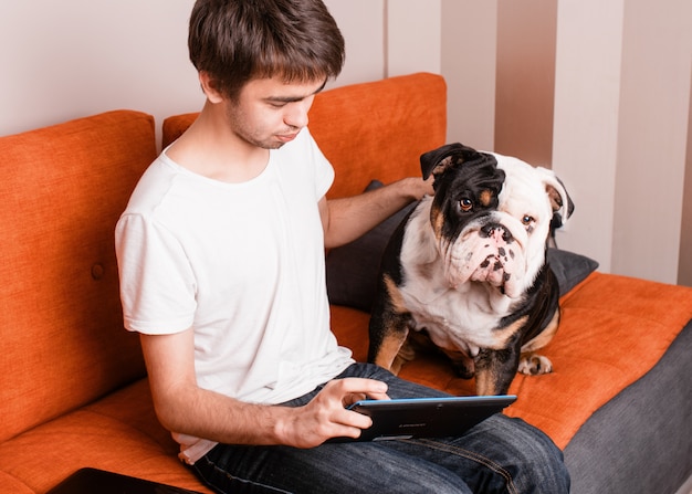 Un ragazzo seduto su un divano a studiare o imparare online sul tablet con il suo cane bianco e nero