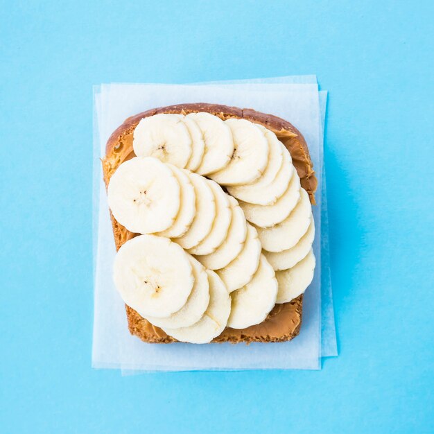한 빵 토스트는 파란색 배경에 바나나 조각 위에 땅콩 버터로 얼룩 져