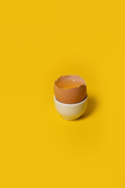 One brown chicken egg in egg cup on yellow background minimal easter concept idea