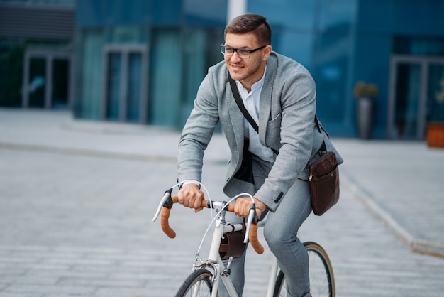 One businessman poses on bicycle at the office building in downtown. Business person riding on eco transport on city street