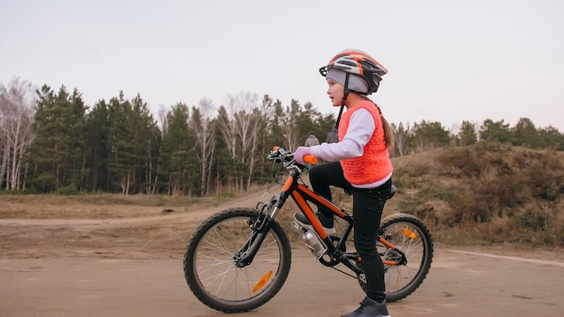 One caucasian children rides bike road track in dirt park girl riding black orange cycle in racetrac