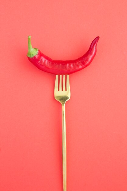 One chili  impaled on a gold fork on red