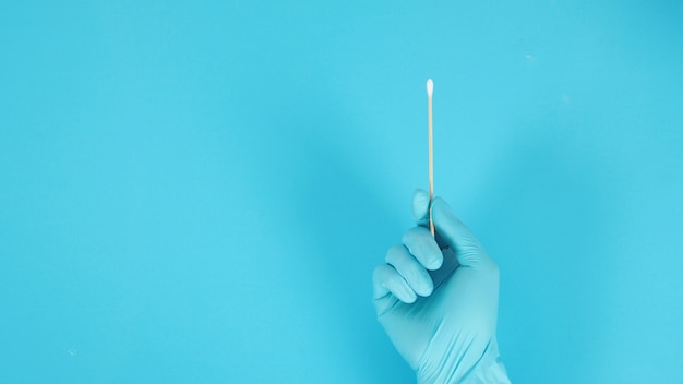 One Cotton stick in hand with blue medical gloves or latex glove on blue background.covid-19 concept