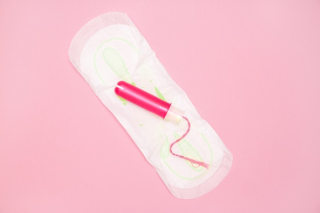 Фото Один хлопковый тампон с розовым аппликатором на менструальной прокладке на розовом.