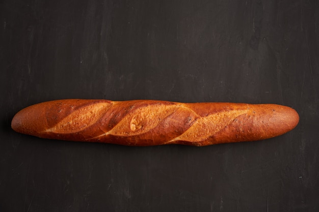 One crispy french baguettes lie dark black table background