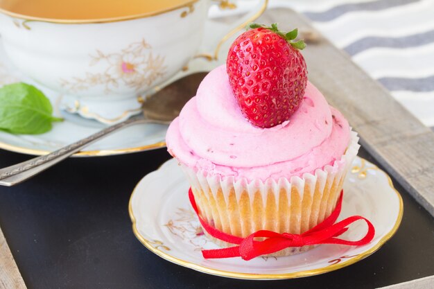 One cupcake with fresh strawberry in plate on wooden table