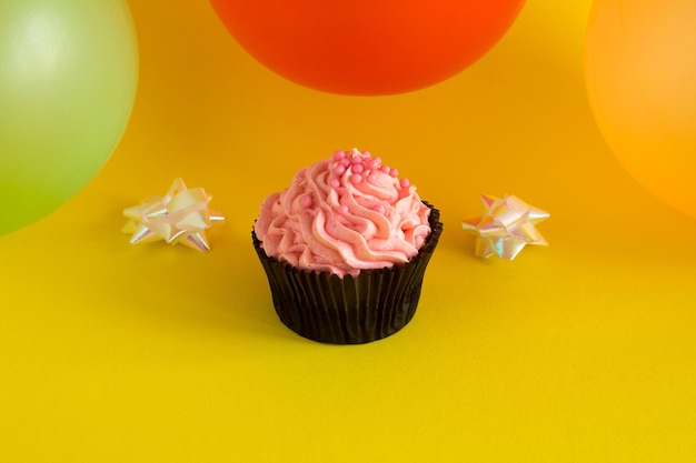 Foto un cupcake con crema rosa e palloncini colorati su sfondo giallo