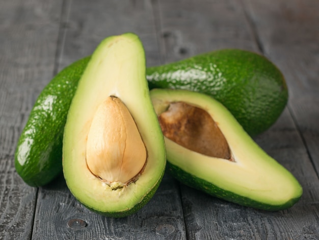 One cut and two whole avocados on a wooden table.