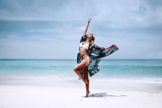 One cute beautiful blonde in a dressed black transparent cape and white swimsuit