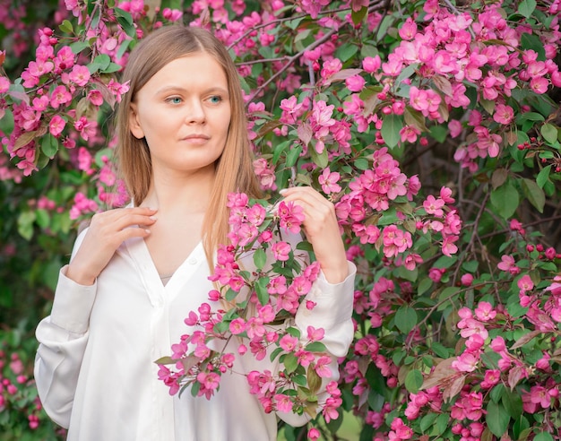 Foto una carina donna bionda pensosa con camicetta bianca tra fiorente con fiori rosa albero di mele