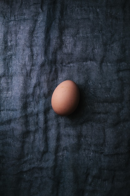 写真 暗い生地の背景に1つの卵。イースター、春、またはエコフードのコンセプト。上面図