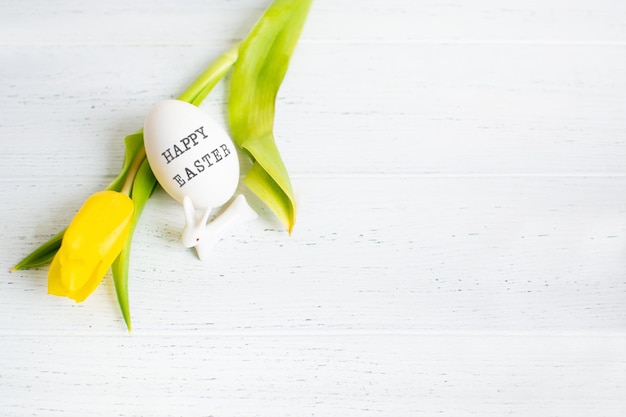 One egg with text happy easter and yellow tulip and white small ceramic bunny