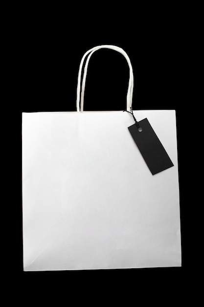 One empty white paper shopping package with blank tag on black close up Copy space