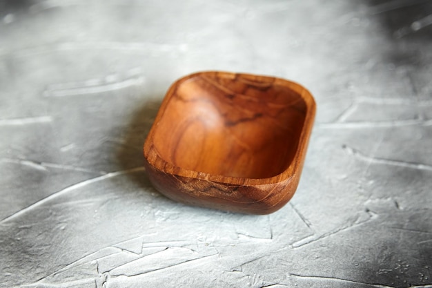 One empty wooden bowl on grey background Single square salad bowl on stone table side view