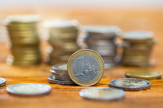 One euro coin on table with others stacked on pile in background