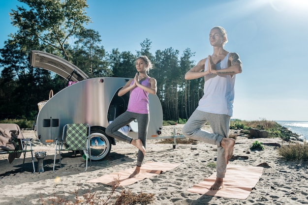 One foot. Loving healthy couple standing on one foot while doing morning yoga near their mobile home