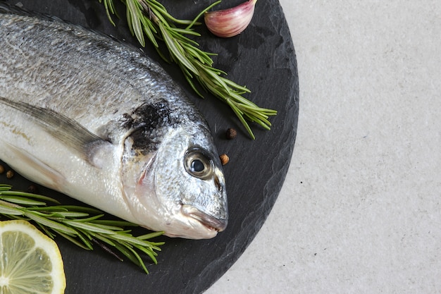 one fresh raw sea organic dorado or sea bream with spices and lemon on a grey background