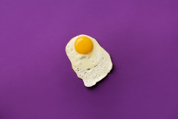 One fried egg on violet paper background