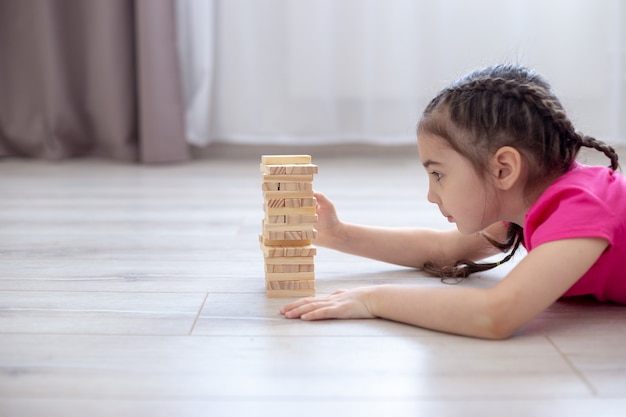 Una ragazza giace sul pavimento nella stanza e gioca al gioco dei blocchi di legno della torre. giochi da tavolo per famiglie