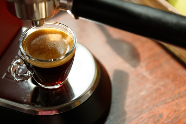 One glass coffee cup with espresso near the window and coffee machine in morning on dark background