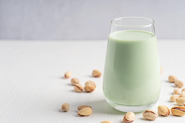 One glass of plant based vegetarian pistachio milk served with seeds on white wooden background