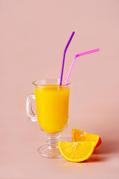One glass with orange juice and cocktail tubes on a beige background copy space
