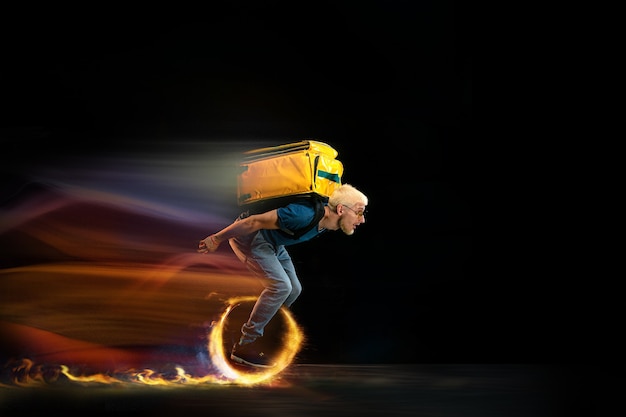 Photo one the go. fast delivery service - deliveryman on unicycle driving with order in fire on dark background. copyspace for ad. super fast shipping of food and goods orders during quarantine.