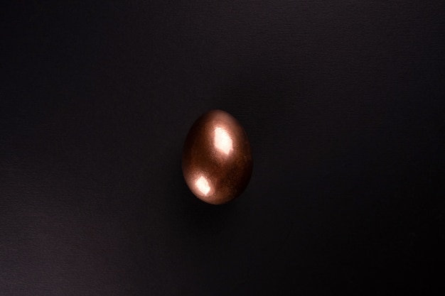 One golden egg lies on a black background, minimalism . Flat lay, Top view, copy space.