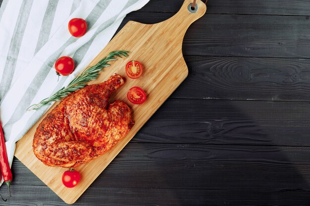 One half of grilled chicken on wooden cutting board close up