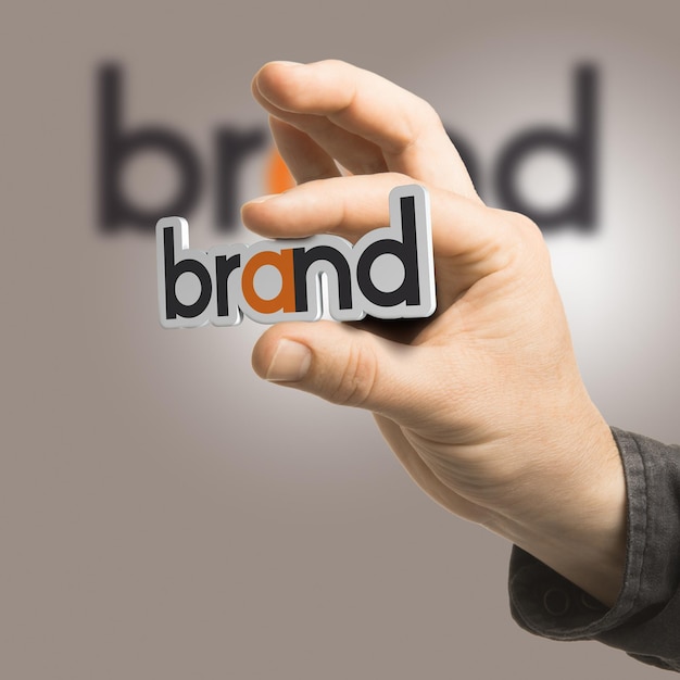 One hand holding the word brand over a beige background. Branding concept. The image is a composition between 2D illustration, 3D rendering and photography